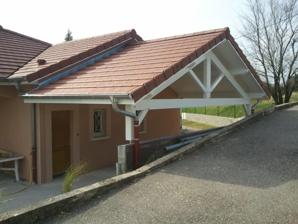 Auvent de Maison en Bois Blanc avec Toiture en Tuiles Auvent en bois blanc avec toit en tuiles rouges attenant à une maison orange, bordé par une allée goudronnée.