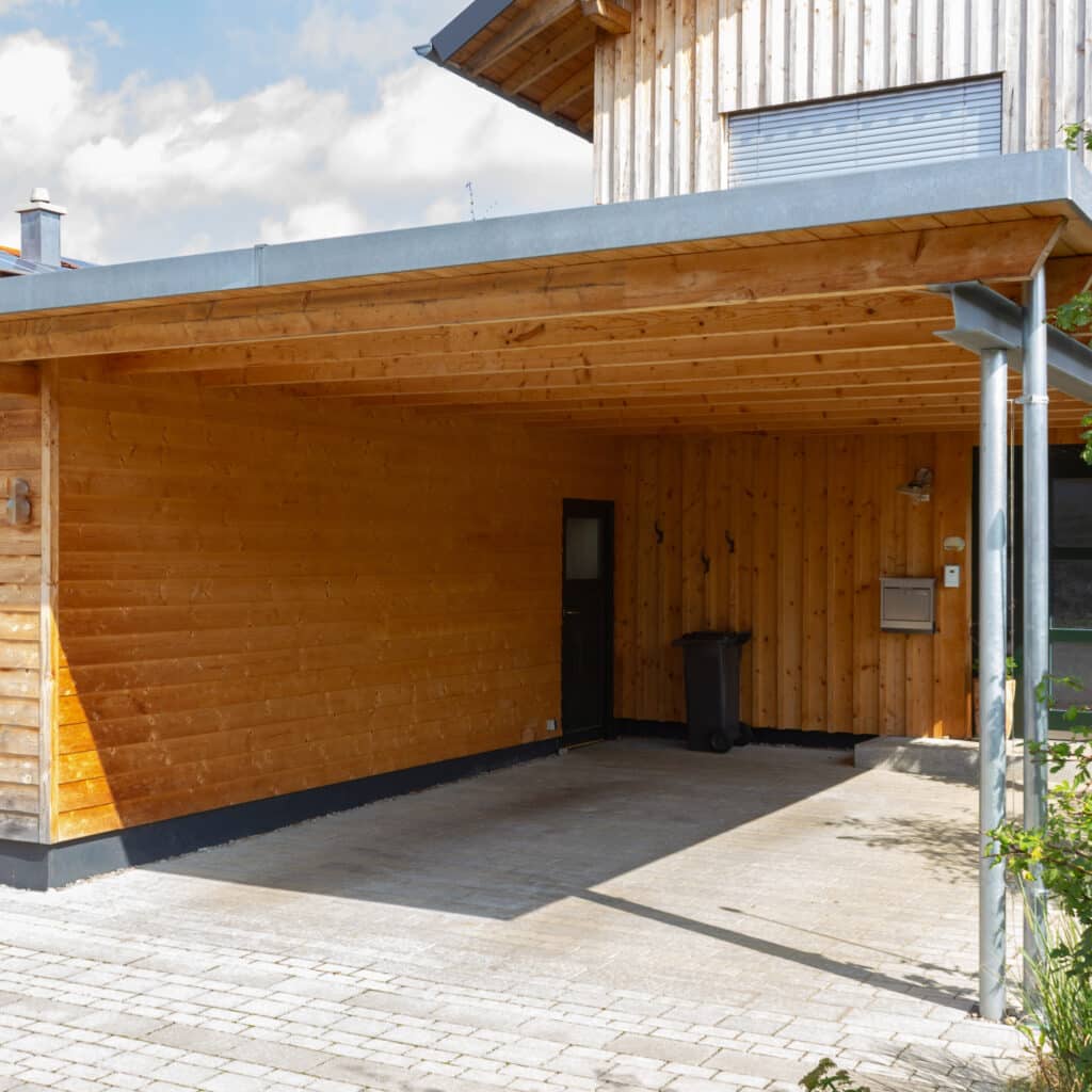 Carport en Bois Moderne : Abri Voiture et Design Naturel Carport moderne en bois naturel avec toit plat et allée pavée devant une maison contemporaine.