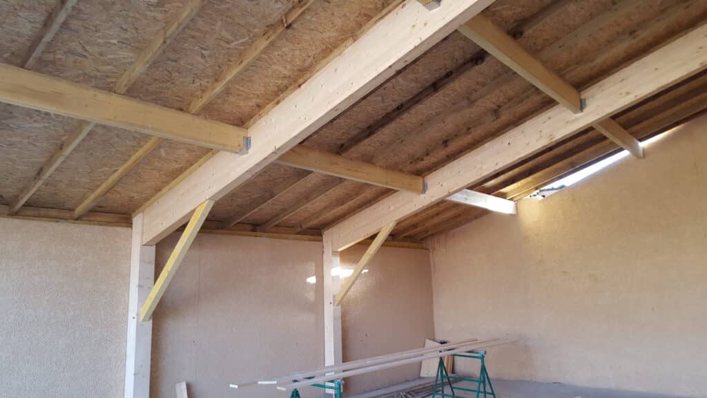 Construction Charpente Bois et Toiture OSB pour Abri Charpente bois apparente, panneaux OSB et contreventements jaunes dans un abri ou garage en construction.