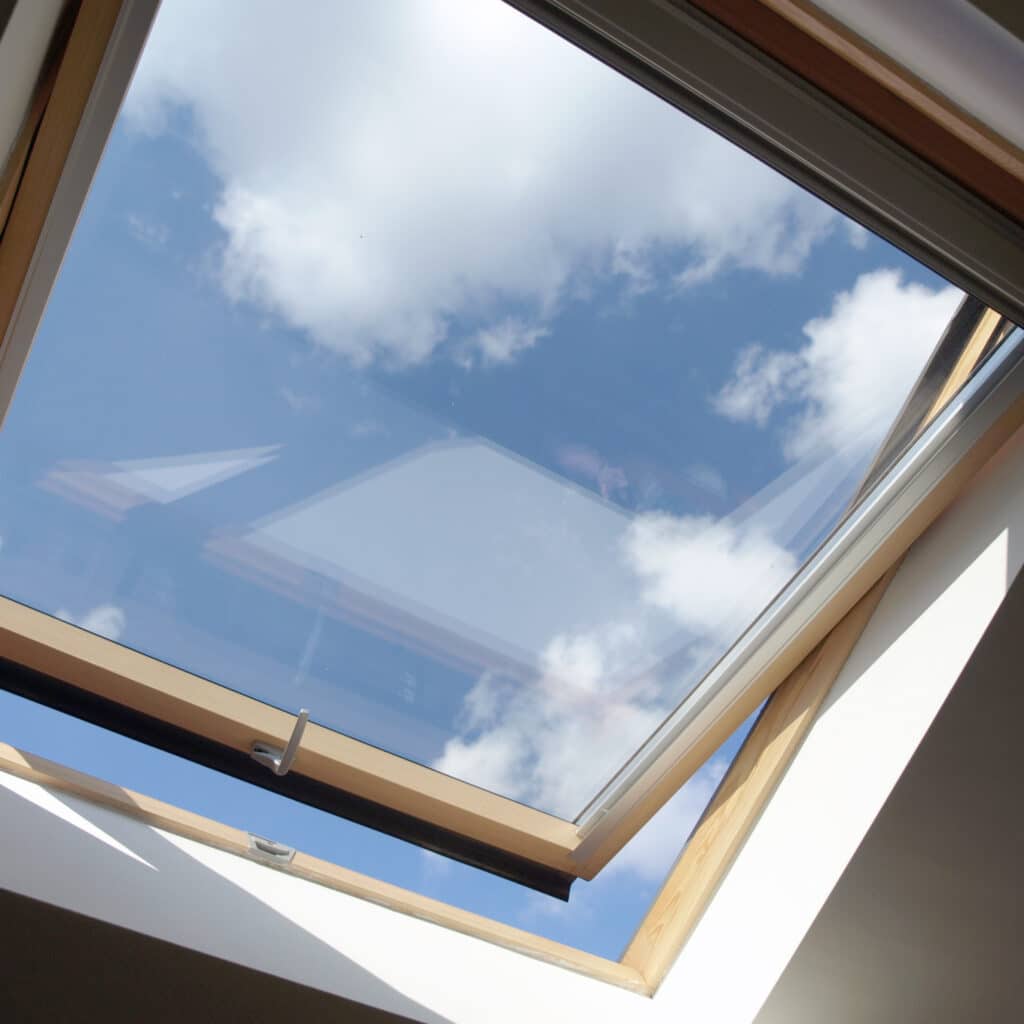 Fenêtre de toit en bois pour une vue sur le ciel bleu Fenêtre de toit en bois ouverte sur un ciel bleu parsemé de nuages blancs, apportant de la lumière naturelle.