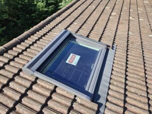 Fenêtre de toit Velux sur toiture en tuiles avec étiquette de marque et raccord d'étanchéité gris.