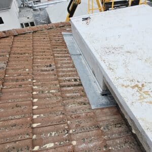 Tuiles en terre cuite et nouveau solin métallique sur une toiture en rénovation avec une structure blanche.